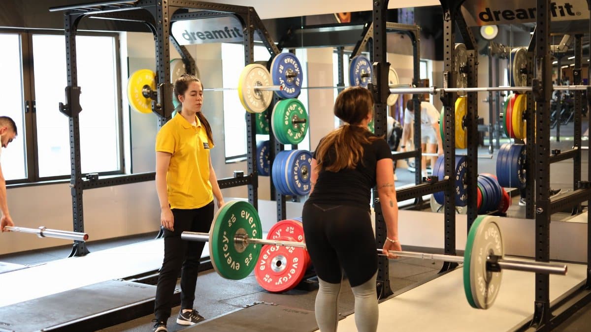 Two women weightlifting in a modern gym with colorful plates, showcasing fitness training.