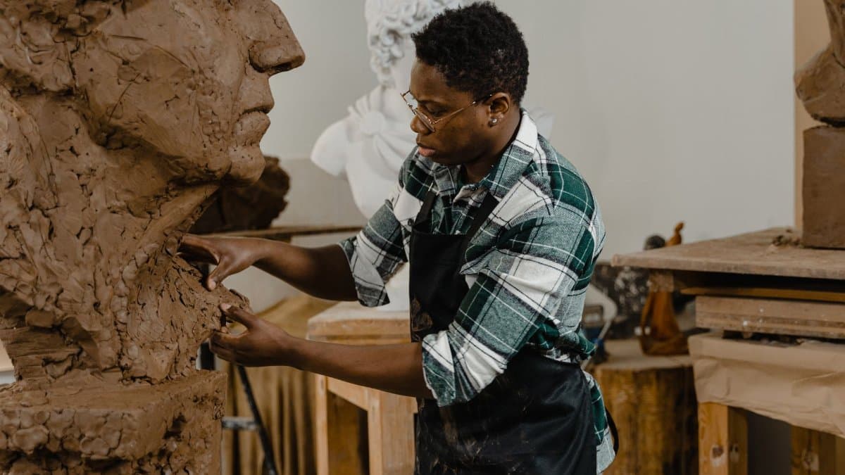 Artist sculpting a large clay bust in an art studio, showcasing creativity and craftsmanship.