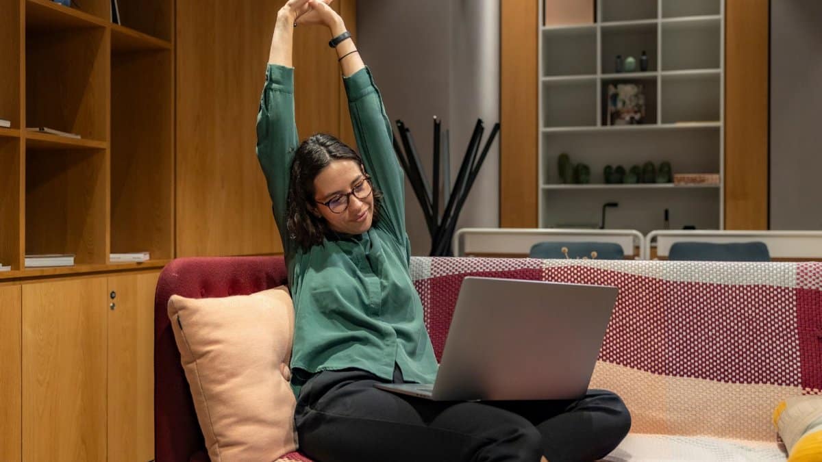 A woman relaxes while working from home on a sofa, showcasing a flexible work environment.