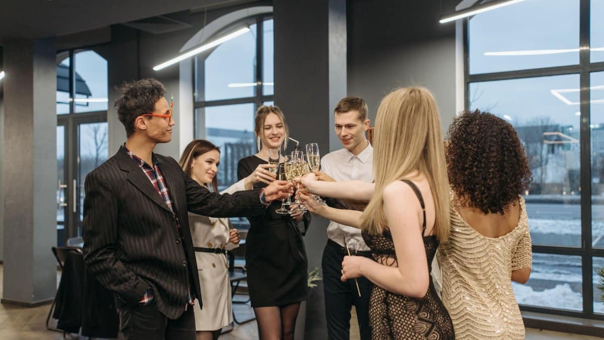 Group of colleagues celebrating indoors by toasting with wine glasses. Diverse office party atmosphere.