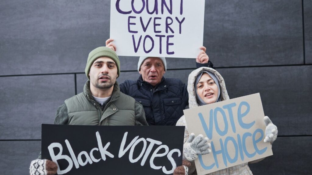 A diverse group of people holding signs advocating for voting rights and equality during a winter outdoor protest.
