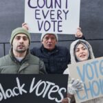 A diverse group of people holding signs advocating for voting rights and equality during a winter outdoor protest.