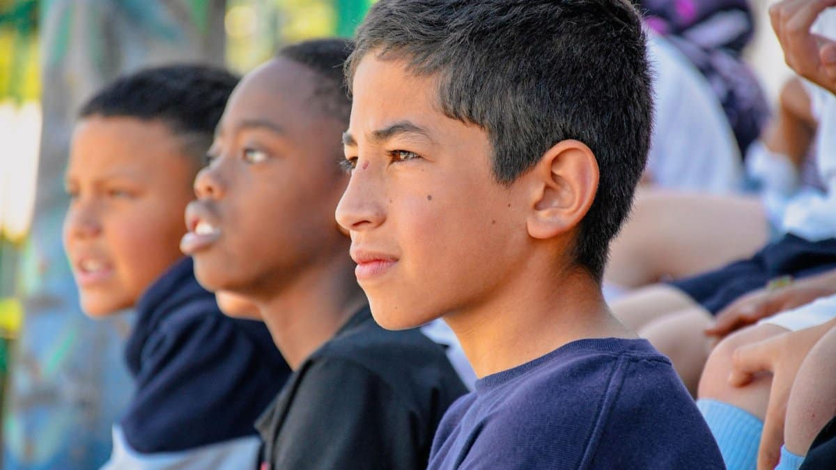 Teenagers of diverse backgrounds attentively watch an outdoor event, showcasing unity and engagement.