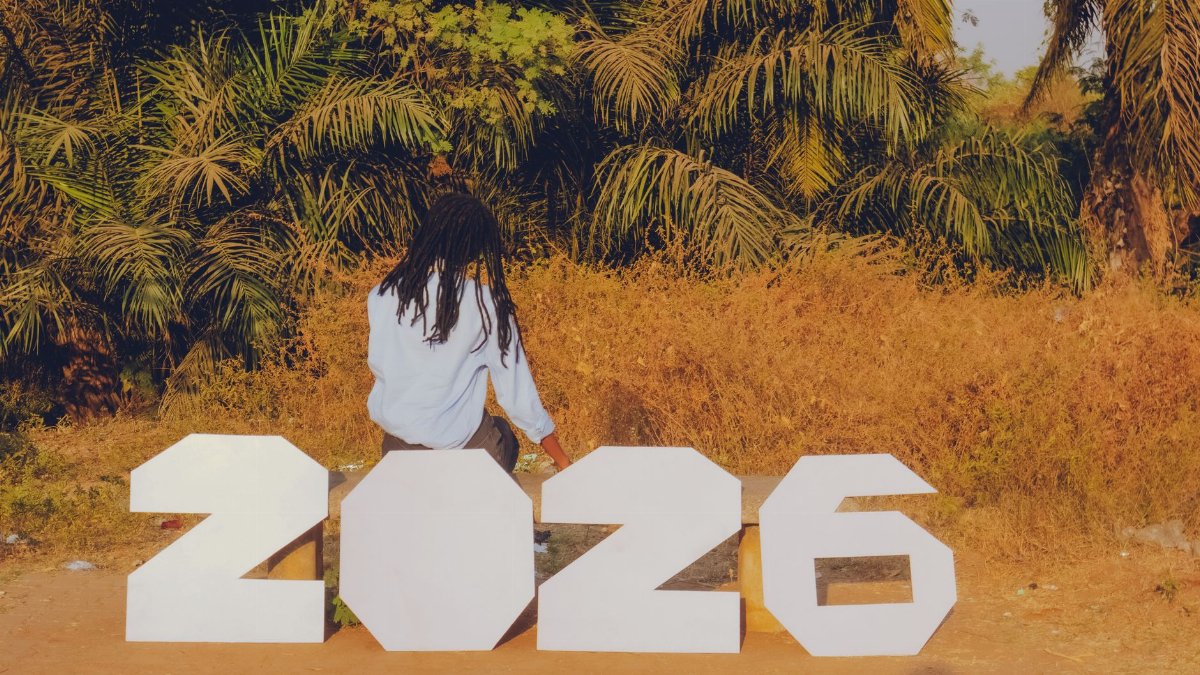 A person sitting outdoors with large numbers spelling 2026, surrounded by tropical foliage.