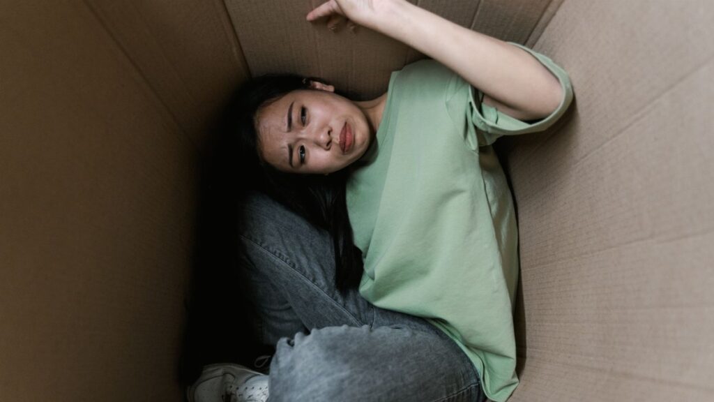 Woman enclosed in a cardboard box, showing signs of stress and fear.