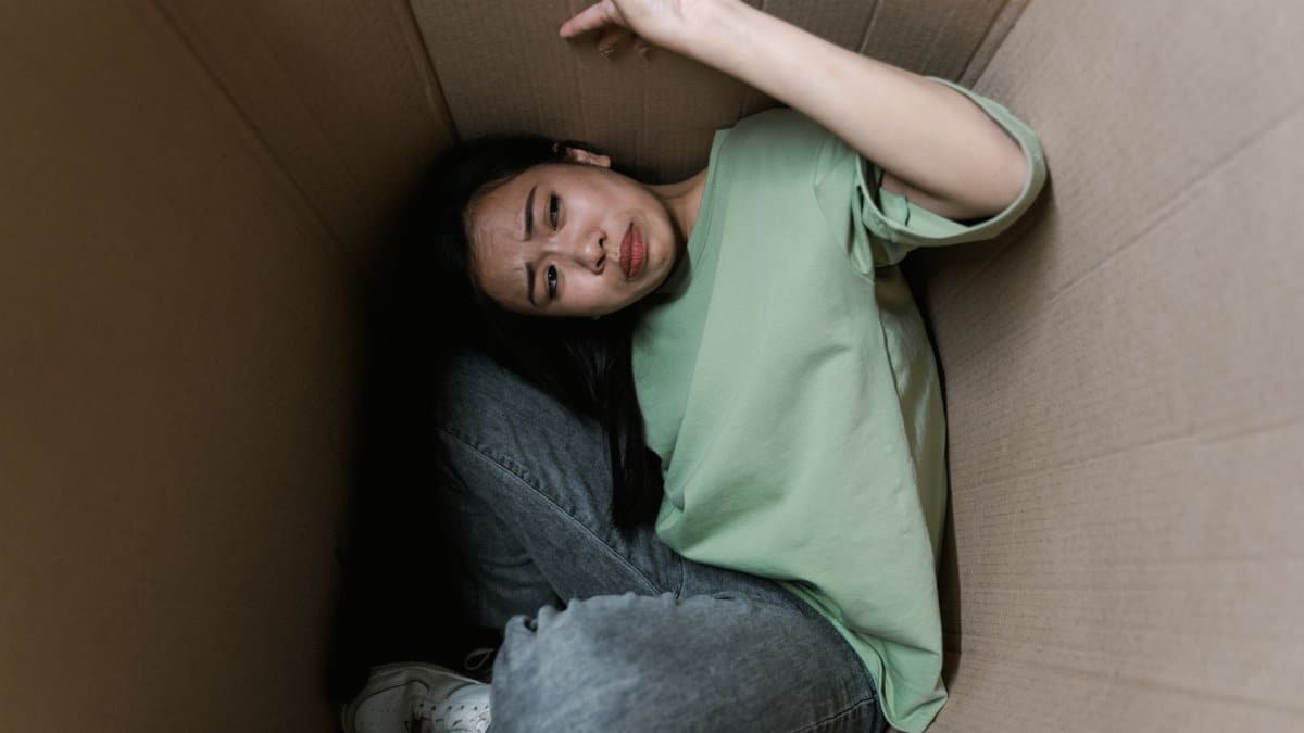 Woman enclosed in a cardboard box, showing signs of stress and fear.