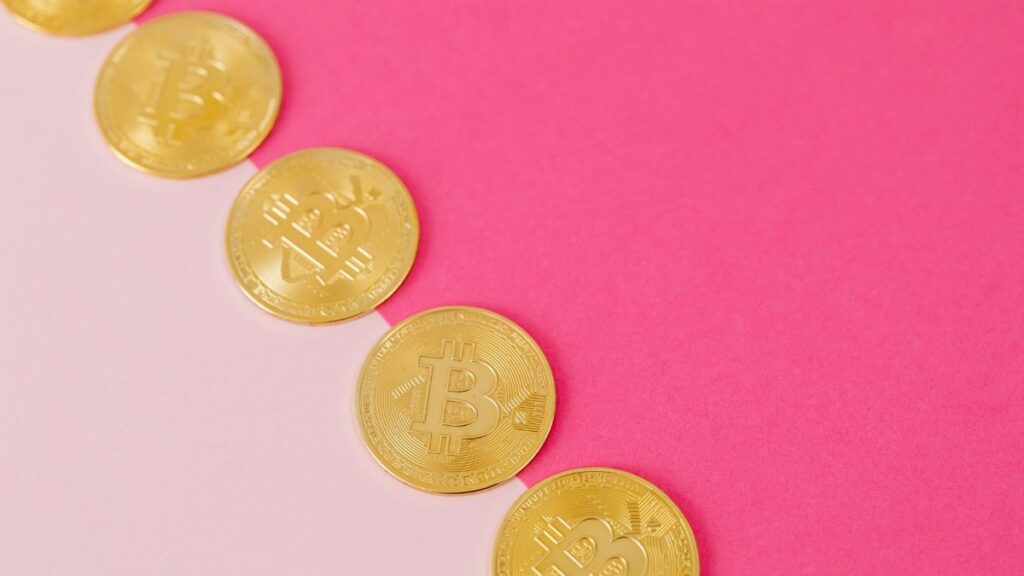 Array of gold bitcoin coins on a striking pink surface, symbolizing modern digital currency.