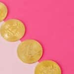 Array of gold bitcoin coins on a striking pink surface, symbolizing modern digital currency.