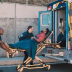 First responders assist an injured man onto a stretcher and into an ambulance during a daytime emergency call.