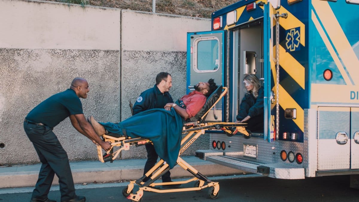 First responders assist an injured man onto a stretcher and into an ambulance during a daytime emergency call.