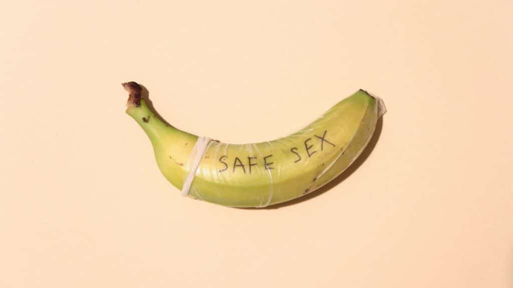 A banana wrapped in a condom for safe sex awareness on a pastel background.
