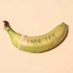 A banana wrapped in a condom for safe sex awareness on a pastel background.