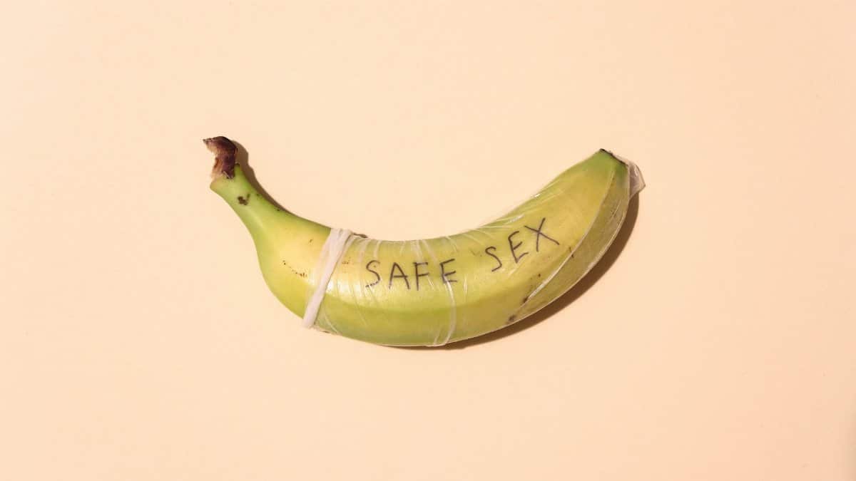 A banana wrapped in a condom for safe sex awareness on a pastel background.