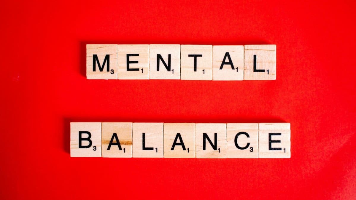 Wooden Scrabble tiles spelling 'Mental Balance' on a vibrant red background.