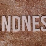Wooden letters spelling 'Kindness' on a textured stone background, conveying a positive message.