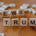 Wooden letter tiles spell 'NEWS' and 'TRUMP' on a wooden table, relating to political discourse.