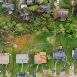 Drone dramatic view of small settlement cottages with ruined roofs and windthrown trees after massive storm