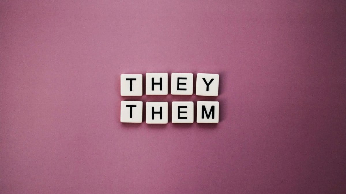 Non-binary pronouns 'they them' displayed with letter tiles on a pink backdrop.