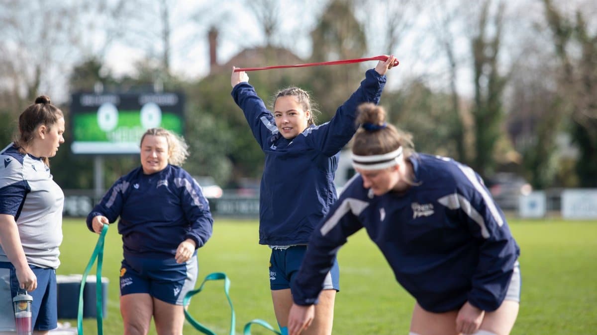 Female rugby team training outdoors with resistance bands on a sunny day.