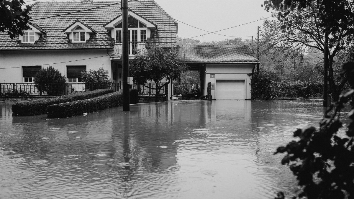 A flooded suburban house surrounded by high water, depicting severe weather impact.