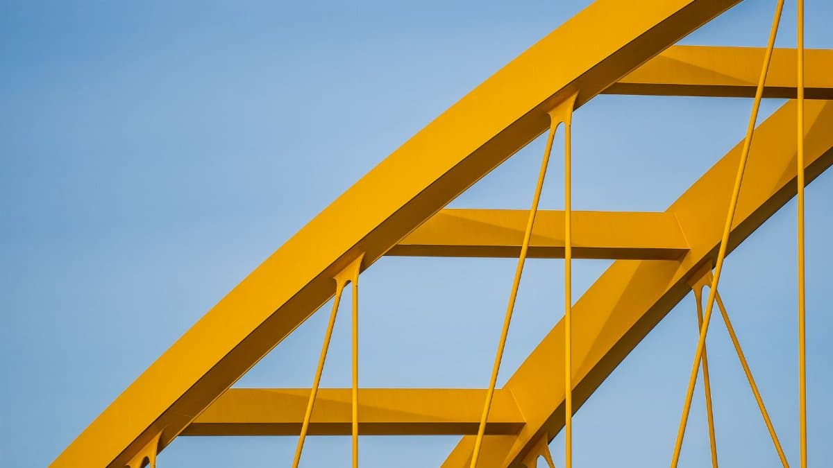 Close-up of a yellow steel bridge with geometric patterns under a clear blue sky.