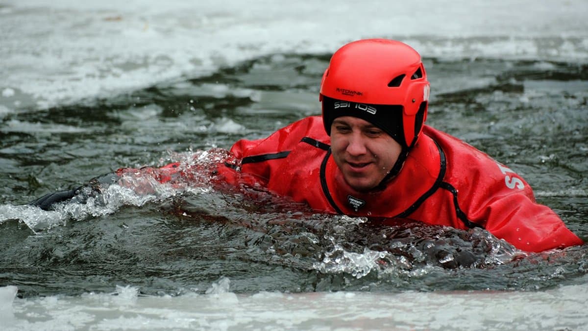 A person in red safety gear practicing ice rescue techniques during winter outdoors.