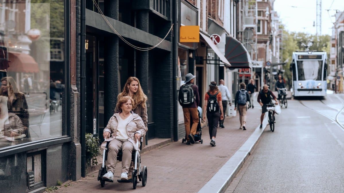 Street view in Amsterdam with people using mobility aids and bikes, reflecting urban life.