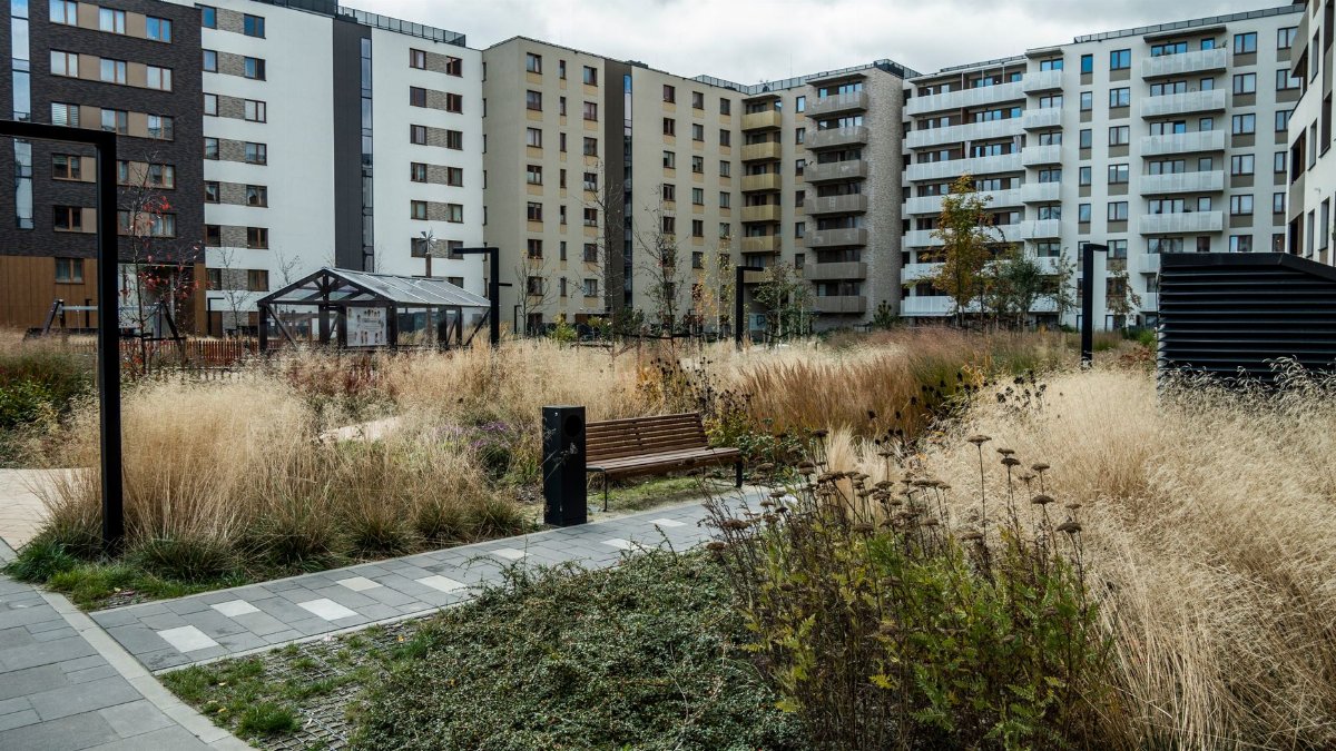 A contemporary apartment complex courtyard featuring rich vegetation and pathways under a cloudy sky.