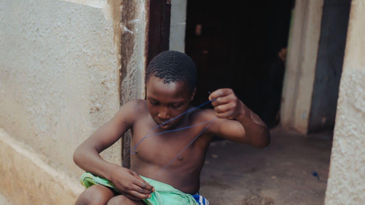 Young boy sewing outdoors, developing practical skills in a natural setting.