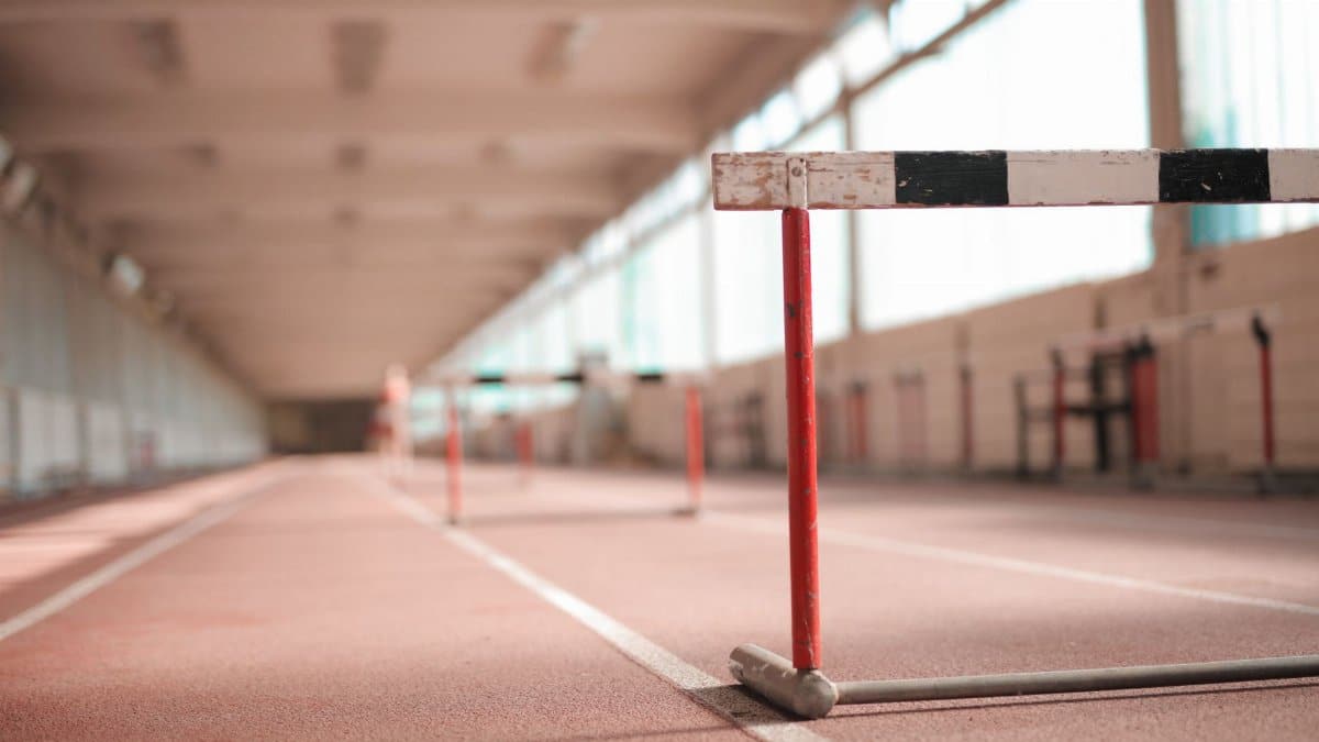 Hurdle painted in white black and red colors placed on empty rubber running track in soft focus