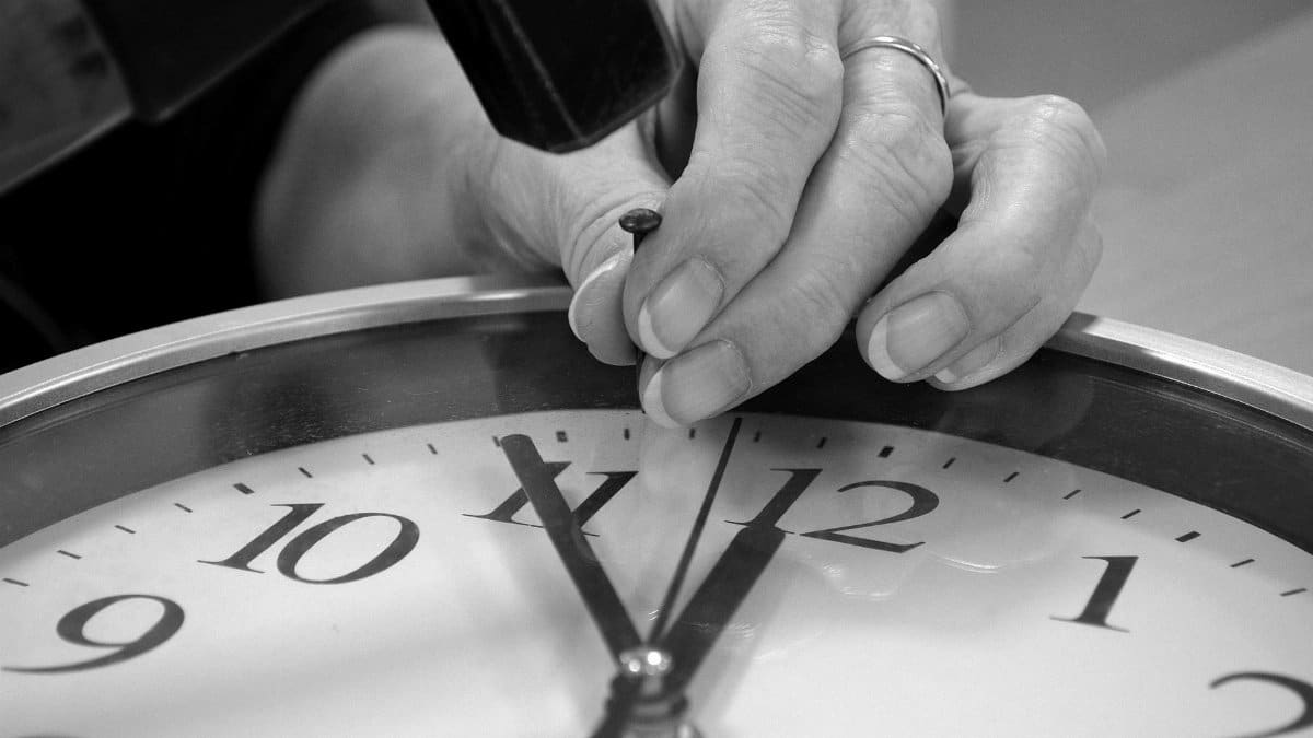 Close-up of hands adjusting a clock with a hammer in monochrome.