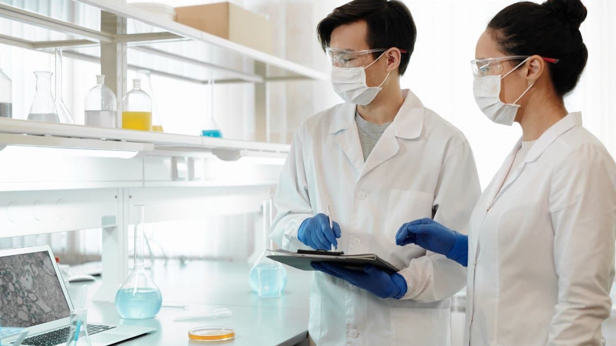 Researchers in laboratory wearing masks, gloves, and goggles working on scientific experiments.