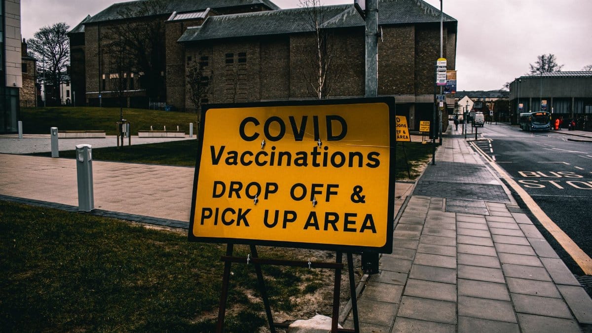 A COVID vaccination drop off and pick up sign on an urban street, highlighting the pandemic's impact.