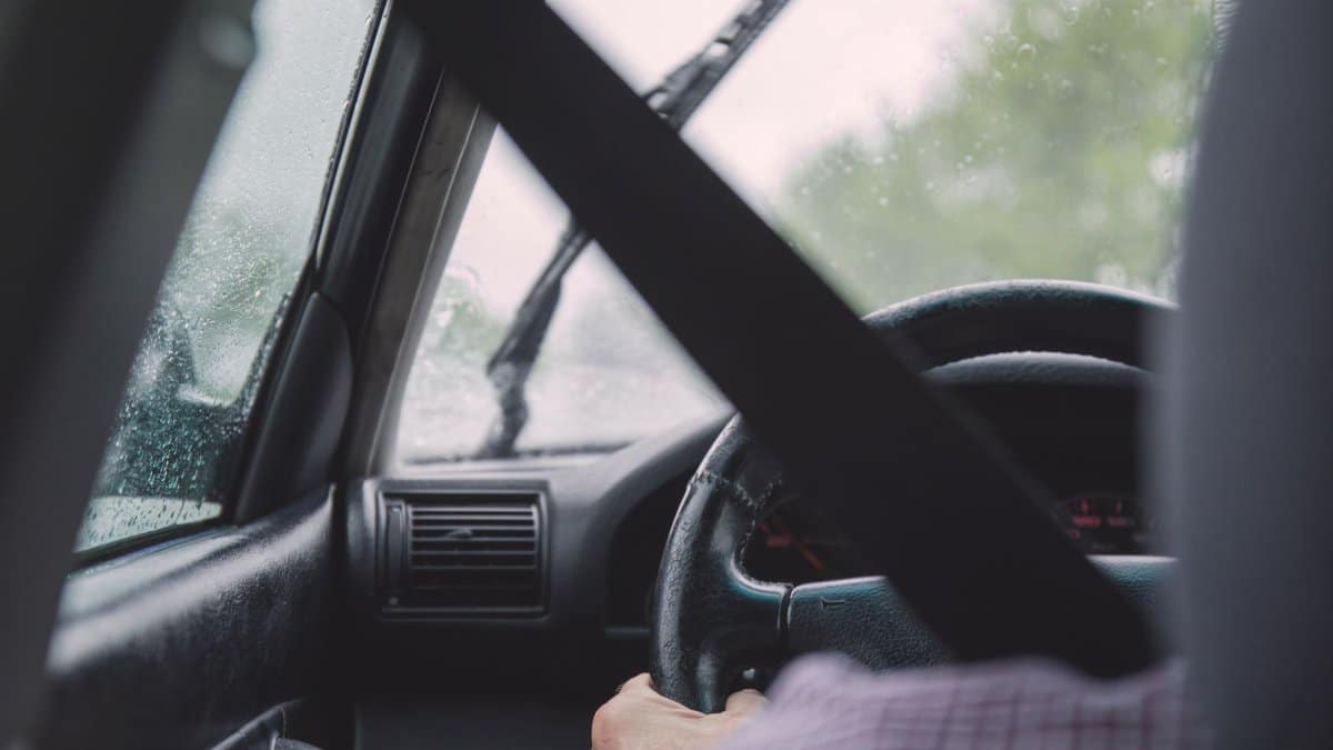 Interior view of a car during rainy weather, emphasizing safety with visible seat belt and driver focused on road.