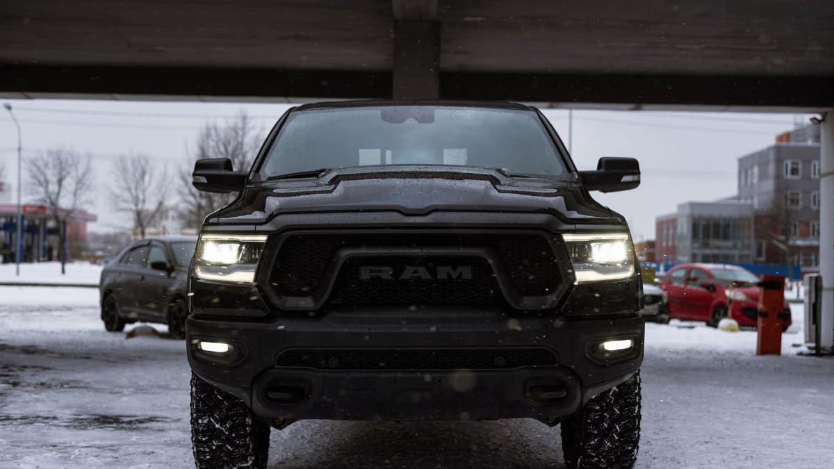 Front view of a black RAM truck parked under a bridge in a snowy urban setting during winter.