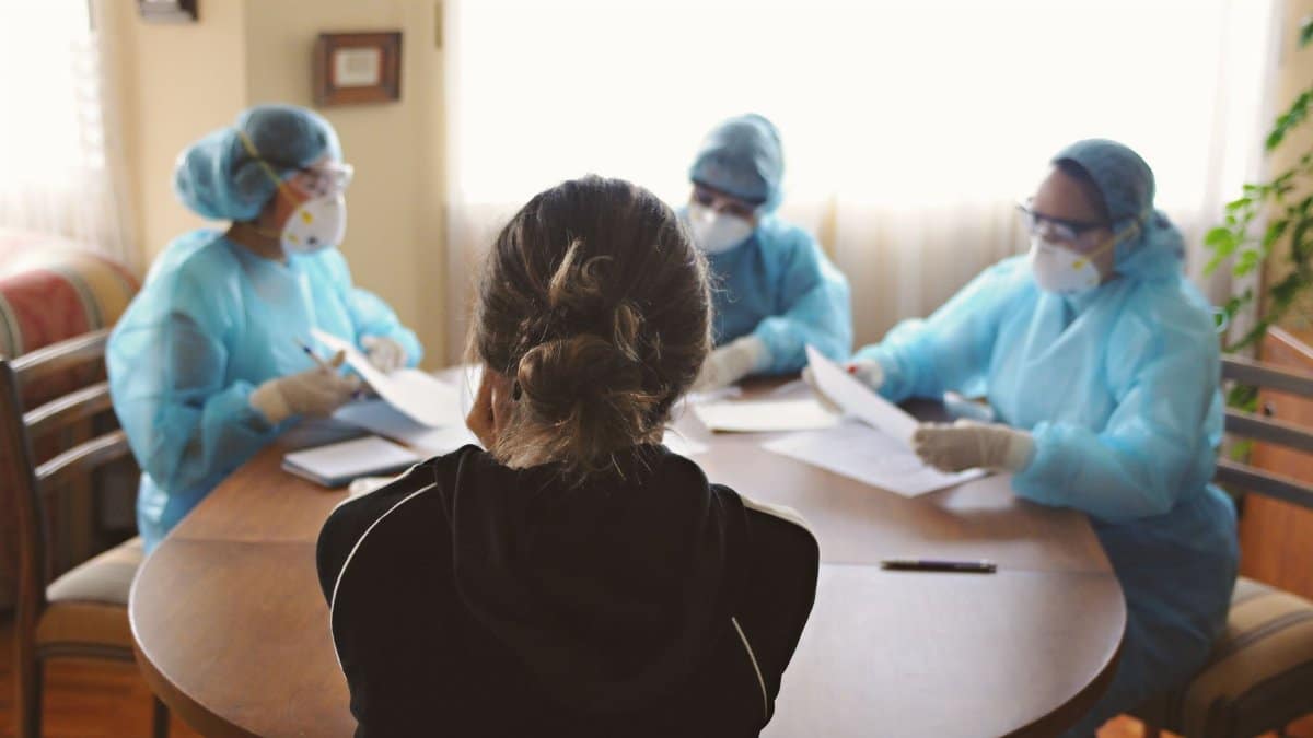 Health professionals in protective gear consulting with a patient indoors, focusing on COVID-19 precautions.