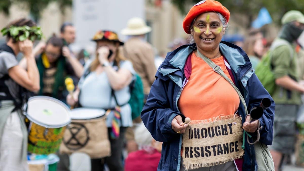 A vibrant protest scene highlighting environmental advocacy with participants carrying signs and drums.