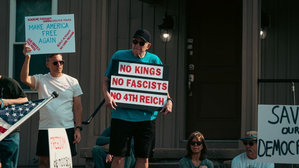 A group of adults protesting with political signs expressing various messages, emphasizing democracy and freedom.