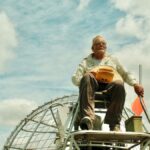 Elderly man navigating an airboat through the Florida Everglades on a sunny day.
