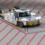Aircraft tug maneuvering on a runway, preparing for plane departure at a busy airport.