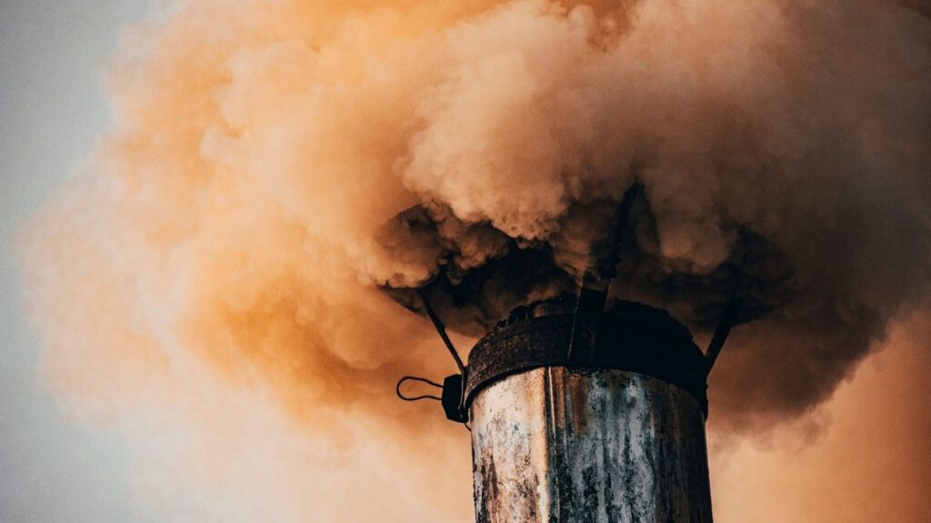 A close-up of a factory smokestack releasing thick smoke into the air, illustrating industrial pollution.