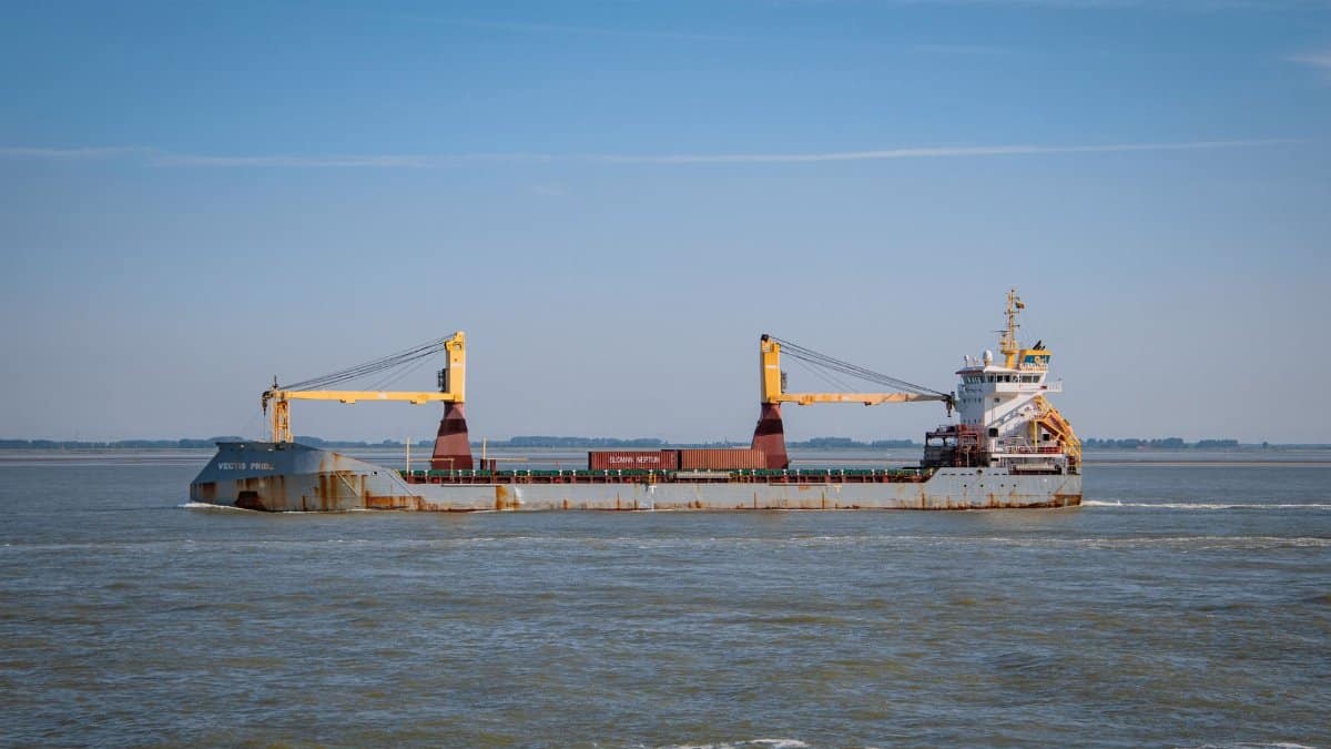 Cargo vessel carrying containers off the coast of Terneuzen in the Netherlands under a clear blue sky.
