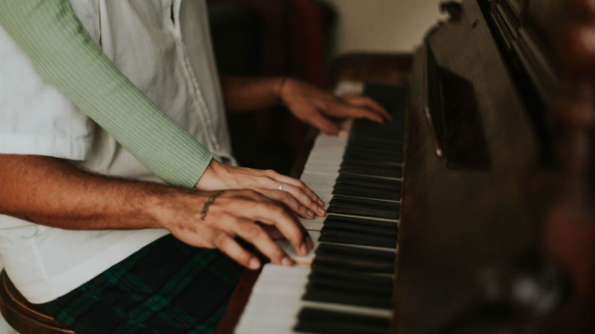 Intimate moment of two people sharing a piano, hands gracefully on keys, creating music jointly.