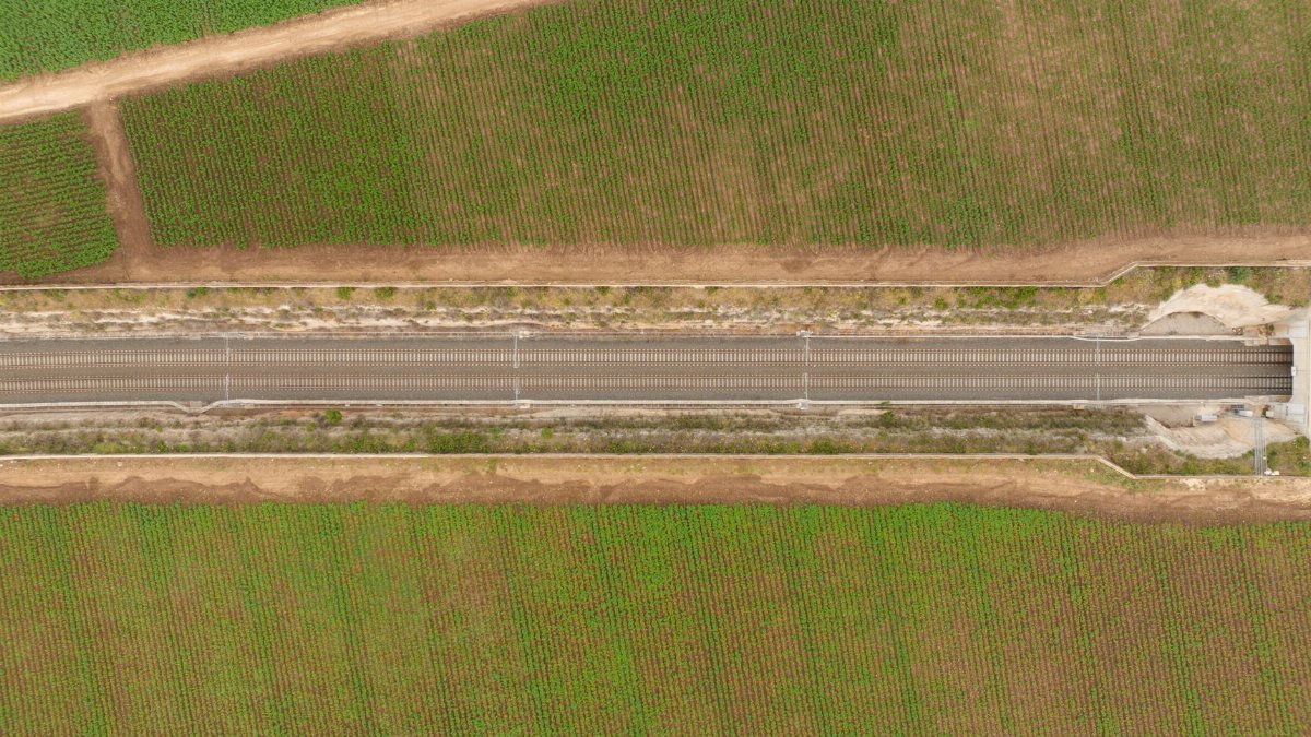 Drone view of a railroad cutting through lush green farmland, illustrating rural infrastructure.