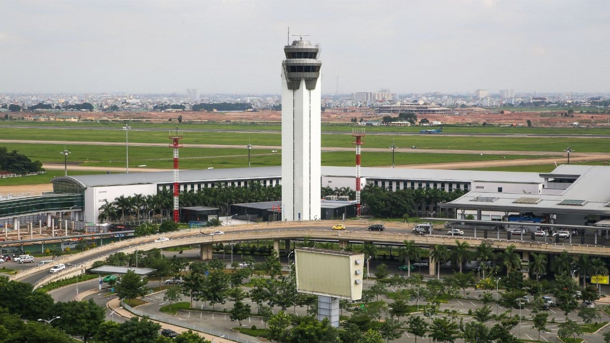 Aerial view of a busy airport with a prominent control tower, surrounded by roads and greenery.