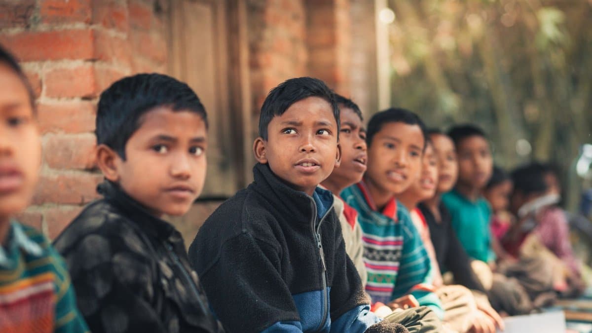A group of children from Bangladesh sitting outdoors, engaged in learning at a rural school.