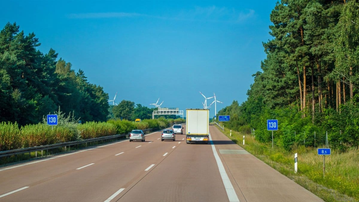 Cars and trucks driving on a highway surrounded by lush greenery and wind turbines.