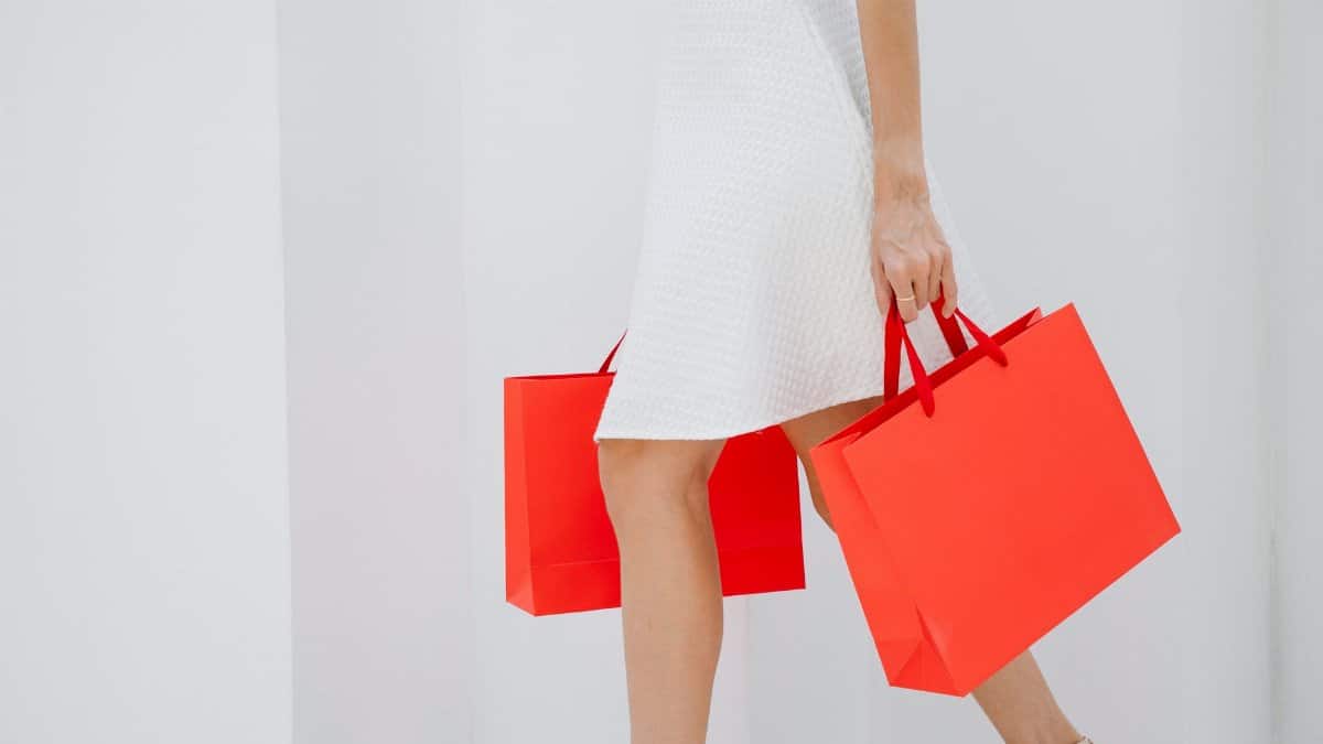 Side view of crop unrecognizable female shopper in dress and high heels walking with purchases in paper bags