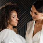 Elegant women smiling and connecting in chic white attire, highlighting friendship.