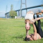 A couple performing acro yoga in a sunny park, showcasing strength and balance.